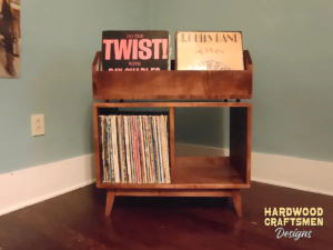 Large solid maple record cabinet featuring two upper vinyl flip bins. The lower section includes two divided storage compartments with backstops, all supported by tapered mid-century legs.
