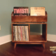 Large solid maple record cabinet featuring two upper vinyl flip bins. The lower section includes two divided storage compartments with backstops, all supported by tapered mid-century legs.