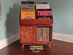 Large solid maple record cabinet with six upper vinyl record flip bins, two divided storage compartments, turntable and media shelves, one hardwood door, and tapered mid-century legs.