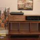Solid walnut record player stand with a dovetail drawer and 3 vinyl storage bin compartments, available from 42 to 72 inches. This Media console features an upper TV shelf above three divided compartments, all on tapered mid-century legs.