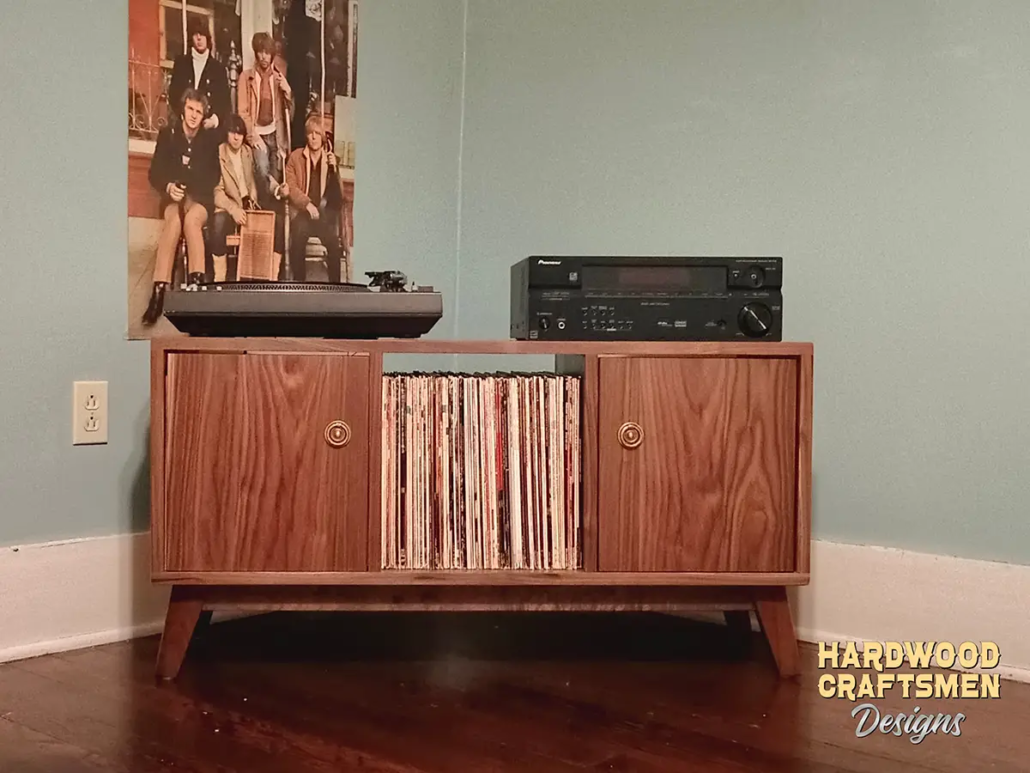 Solid walnut media console, available from 42 to 72 inches, featuring an upper TV shelf above three divided storage compartments, with two outer hardwood doors covering the side compartments, all on tapered mid-century legs.
