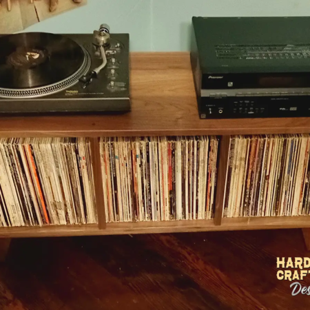 An elevated view of a low-profile solid walnut media console, available from 42 to 72 inches, featuring an upper TV shelf, two media shelves, and three divided storage compartments, all supported by tapered mid-century legs.