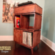 Solid cherry record storage cabinet with dovetail drawers, with upper turntable shelf, dovetail drawer, four divided storage compartments, one lower hardwood door, and tapered mid-century legs.