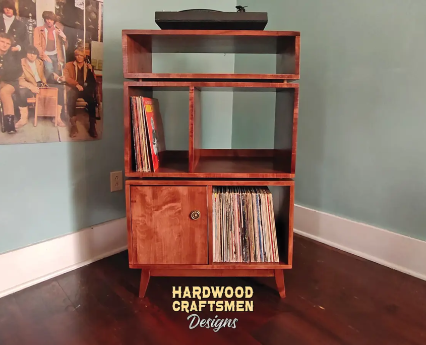 Solid cherry record player cabinet with Audio Bays featuring a turntable shelf with a media compartment below, four storage compartments with one lower door on the left, and tapered mid-century legs.