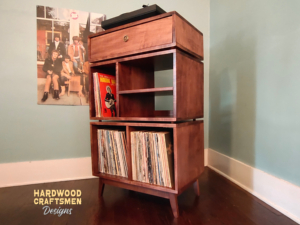 Tall solid hardwood maple record cabinet with upper turntable shelf, modular dovetail drawer, four divided storage compartments, media equipment shelves, and tapered mid-century legs.