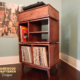 Tall solid hardwood maple record cabinet with upper turntable shelf, modular dovetail drawer, four divided storage compartments, media equipment shelves, and tapered mid-century legs.