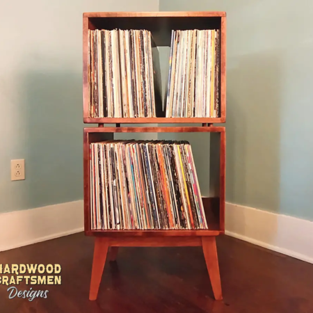 Narrow solid maple record stand featuring an upper turntable and media equipment shelf. The lower section includes two open divided storage compartments stacked vertically, supported by tapered mid-century legs.