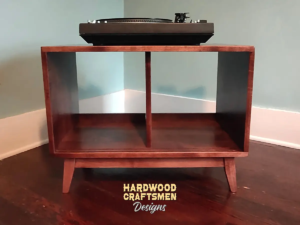Low profile solid cherry record cabinet featuring an upper turntable and media equipment shelf. The lower section includes a media cabinet with two open divided storage compartments, supported by tapered mid-century legs.
