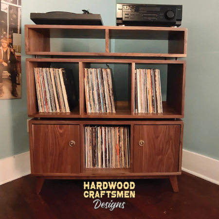 Solid walnut vinyl record storage cabinet featuring two upper side-by-side turntable and media compartments. The lower section includes six divided storage compartments with two outer doors on the bottom level, all supported by tapered mid-century legs.