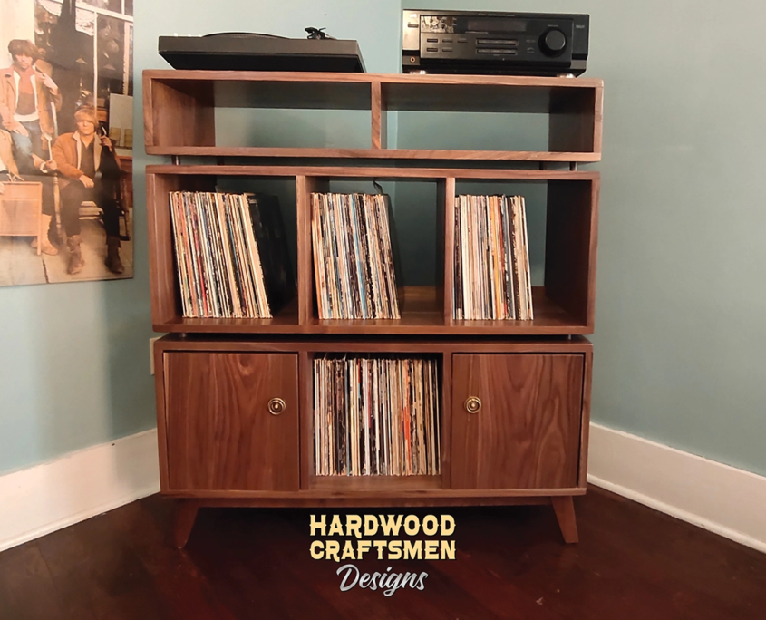 Large solid walnut record player stand featuring two upper side-by-side turntable and media compartments. The lower section includes six divided storage compartments with two outer doors on the bottom level, all supported by tapered mid-century legs.