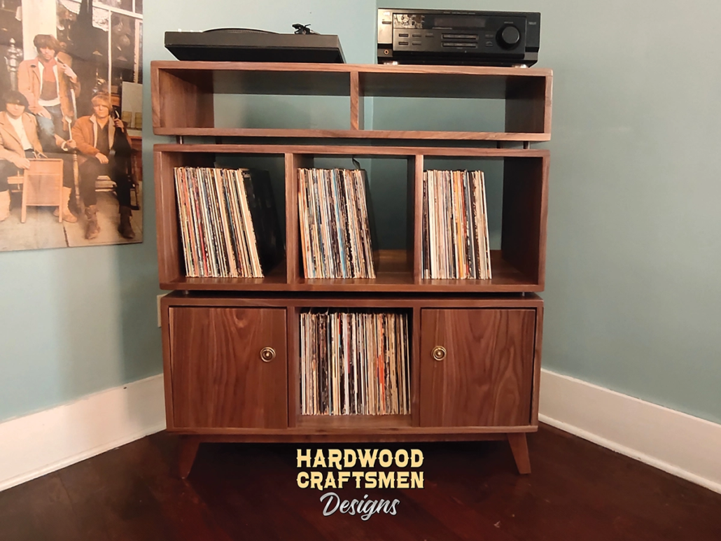 Solid walnut record cabinet featuring two upper side-by-side turntable and media compartments. The lower section includes six divided storage compartments with two outer doors on the bottom level, all supported by tapered mid-century legs.