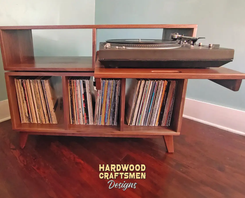 Large solid walnut media console, available from 42 to 72 inches, featuring an upper TV shelf. Below, two media compartments one housing a protruding turntable pull-out shelf directly above three divided storage compartments, all on tapered mid-century legs.