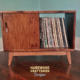 Solid cherry record player cabinet with a turntable shelf, 2 storage bins, 2 sliding doors, and tapered wooden legs.