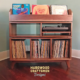 Record player cabinet in solid walnut features 3-to-5 storage compartments below 3-to-5 LP flip bins. This vinyl stand 3-tier is available from 42-to-70-inches, all on tapered mid-century legs.