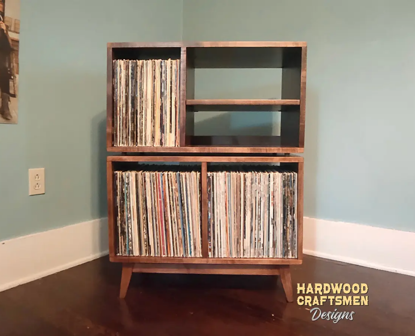 Solid wood record player cabinet with audio shelves featuring a turntable and media shelves, four open vinyl storage compartments, and tapered mid-century legs.