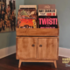 Large solid maple record cabinet with 6 vinyl flip bins, 2 storage compartments, 2 hinged doors, and tapered wooden legs.
