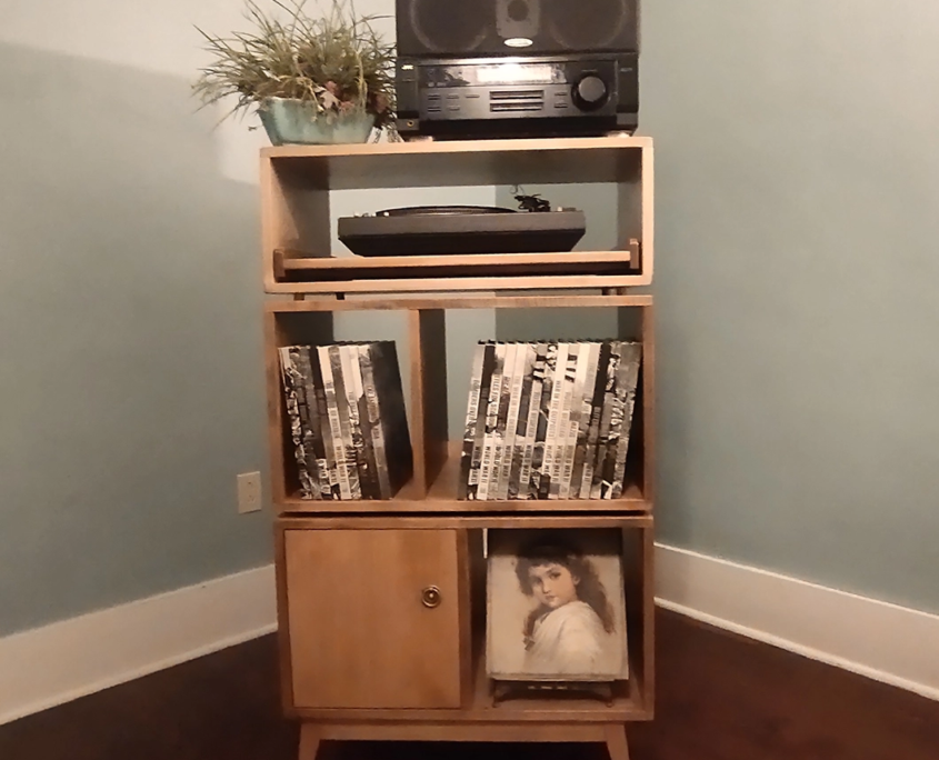 Large tall solid maple record cabinet with upper speaker shelf, pull-out turntable shelf, four grid storage compartments, one lower left door, and tapered mid-century legs.