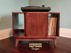 Low profile solid maple mid-century style record cabinet featuring an upper turntable and media equipment shelf. The lower section includes a media cabinet with two open sliding doors and two divided storage compartments.
