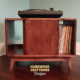 Low profile solid maple mid-century style record cabinet featuring an upper turntable and media equipment shelf. The lower section includes a media cabinet with two open sliding doors and two divided storage compartments.