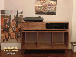 Large solid walnut media console, available from 42 to 72 inches, featuring an upper TV shelf. Below is a drawer and adjacent media compartment above three open storage compartments revealing the interior walls, all on tapered mid-century legs.