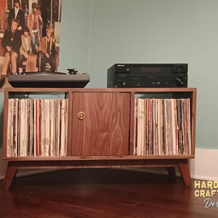 Low-profile solid walnut vinyl record storage cabinet with doors, available from 42 to 72 inches, featuring an upper TV shelf above three divided storage compartments, with one center hardwood door covering the center compartment, all on tapered mid-century legs.