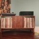Low-profile solid walnut vinyl record storage cabinet with doors, available from 42 to 72 inches, featuring an upper TV shelf above three divided storage compartments, with one center hardwood door covering the center compartment, all on tapered mid-century legs.