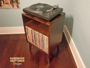 Small solid cherry wood media console with an upper turntable shelf, a media compartment below and a lower vinyl storage compartment, on tapered mid-century legs.
