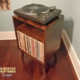 Small solid cherry wood media console with an upper turntable shelf, a media compartment below and a lower vinyl storage compartment, on tapered mid-century legs.