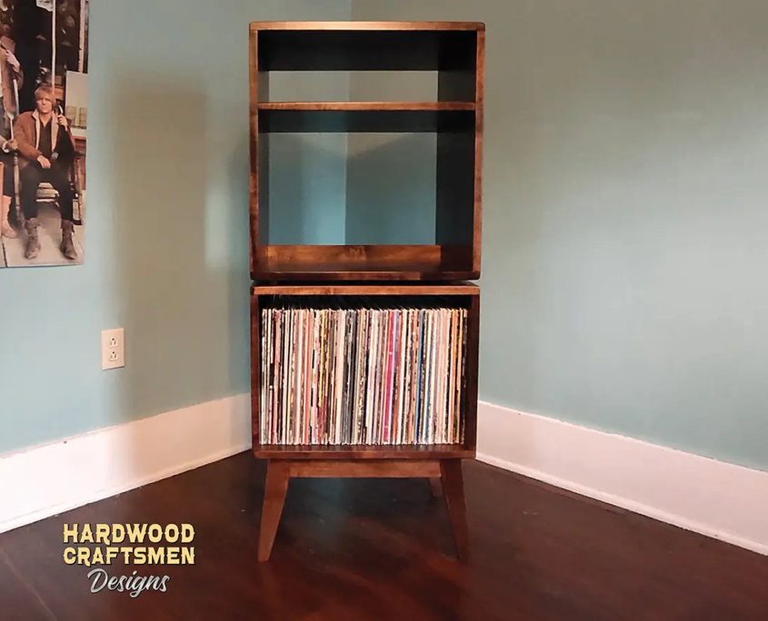 Tall, narrow solid cherry media console featuring an upper turntable shelf. The lower section includes a media compartment above two open storage compartments stacked vertically, supported by tapered mid-century legs.