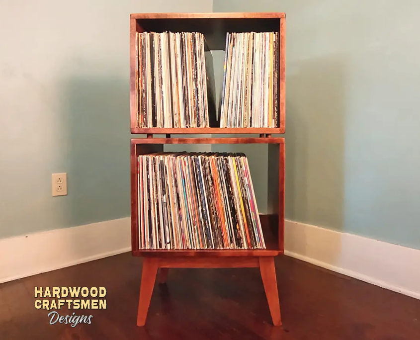 Narrow solid maple record cabinet featuring an upper turntable and media equipment shelf. The lower section includes two open divided storage compartments stacked vertically, supported by tapered mid-century legs.