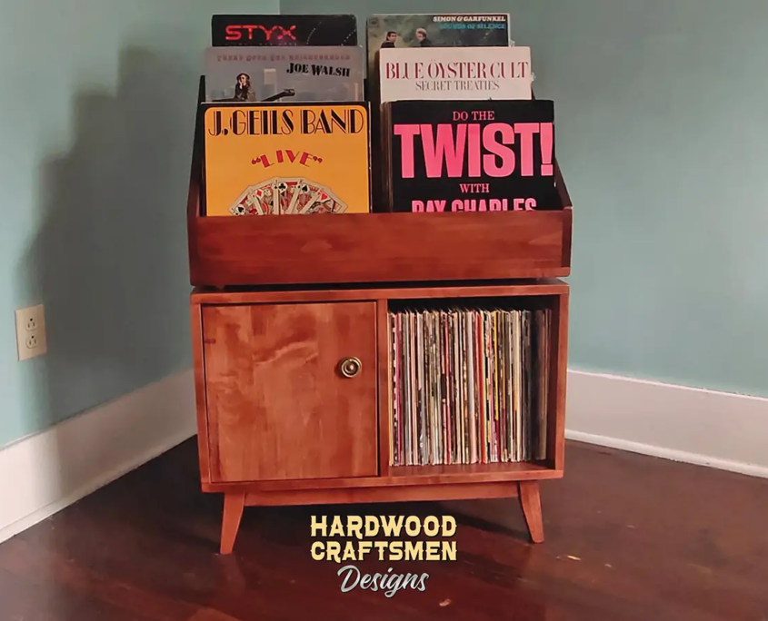 Large solid cherry record cabinet featuring six upper vinyl flip bins. The lower section includes two divided storage compartments, with a door over the bottom left section, all supported by tapered mid-century legs.