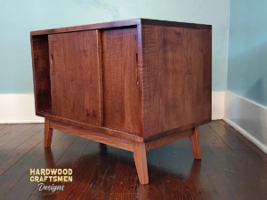 Solid cherry wood audio storage cabinet featuring an upper turntable and media equipment shelf. The lower section includes a media cabinet with two sliding doors and two divided storage compartments.