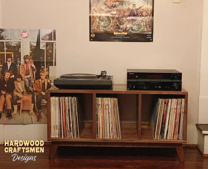 Low-profile solid walnut media console, available from 42 to 72 inches, featuring an upper TV shelf, two media shelves, and three divided storage compartments, all supported by tapered mid-century legs.