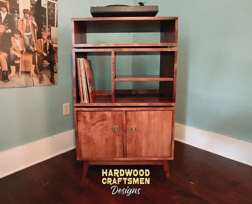 Large, tall solid maple record cabinet, available from 28 to 42 inches wide, featuring an upper turntable shelf. Below is a media compartment above four storage compartments arranged in a 2x2 grid with two bottom doors, all on tapered mid-century legs.