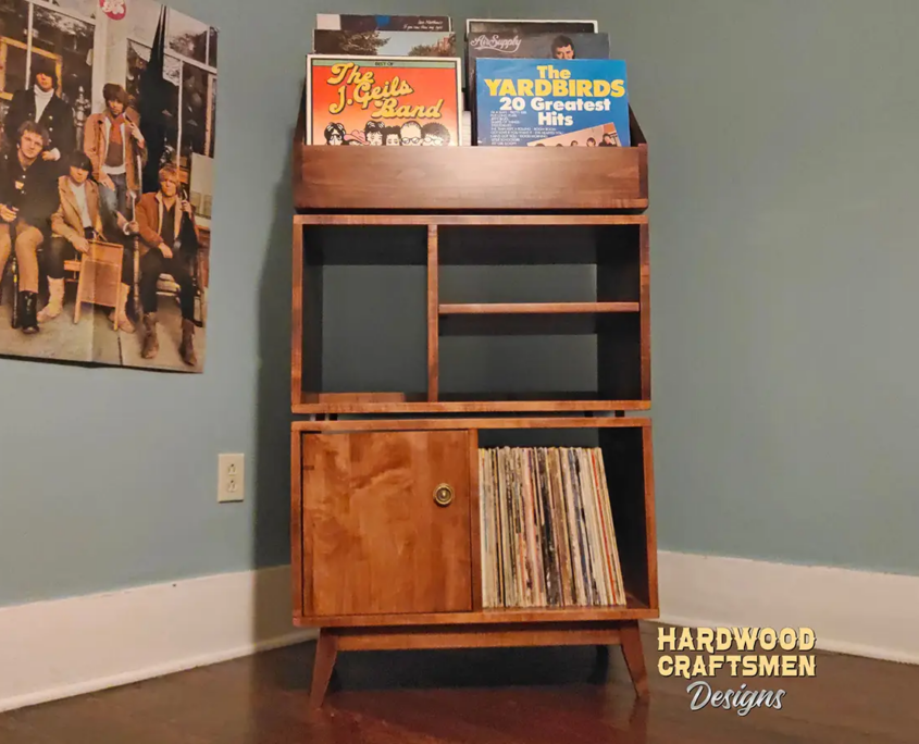 Tall solid maple record stand with six upper vinyl flip bins, four divided storage compartments, turntable and media shelves, hardwood door, and tapered mid-century legs.