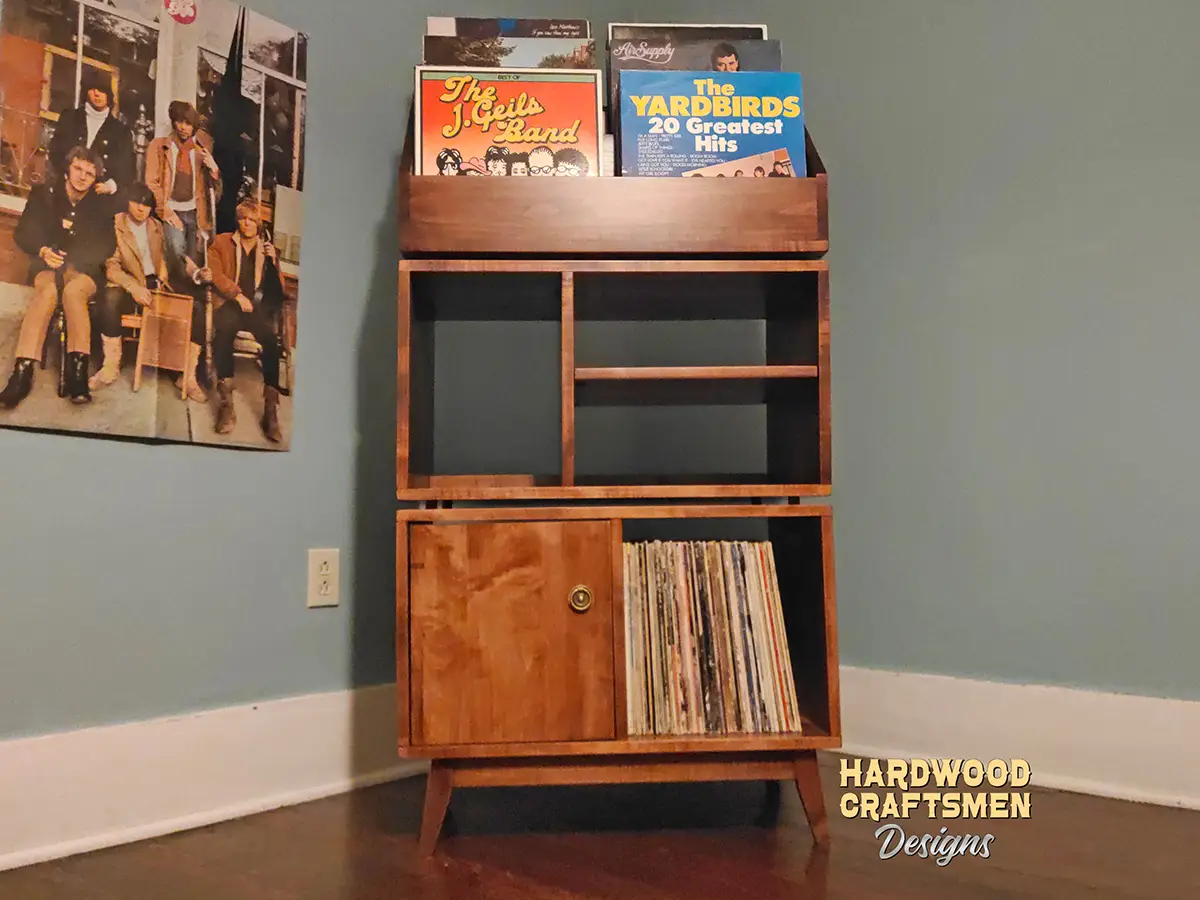 Tall solid maple record stand with six upper vinyl flip bins, four divided storage compartments, turntable and media shelves, hardwood door, and tapered mid-century legs.