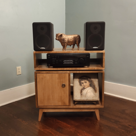 Solid maple media cabinet with vinyl storage & doors featuring an upper speaker shelf. The lower section includes two divided storage compartments, with a door on the bottom left compartment, all supported by tapered mid-century legs.