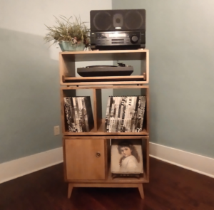 Large 2x3 solid wood record stand featuring a speaker shelf and a turntable pull-out shelf below, four storage compartments with a door on the bottom left, and tapered mid-century legs.