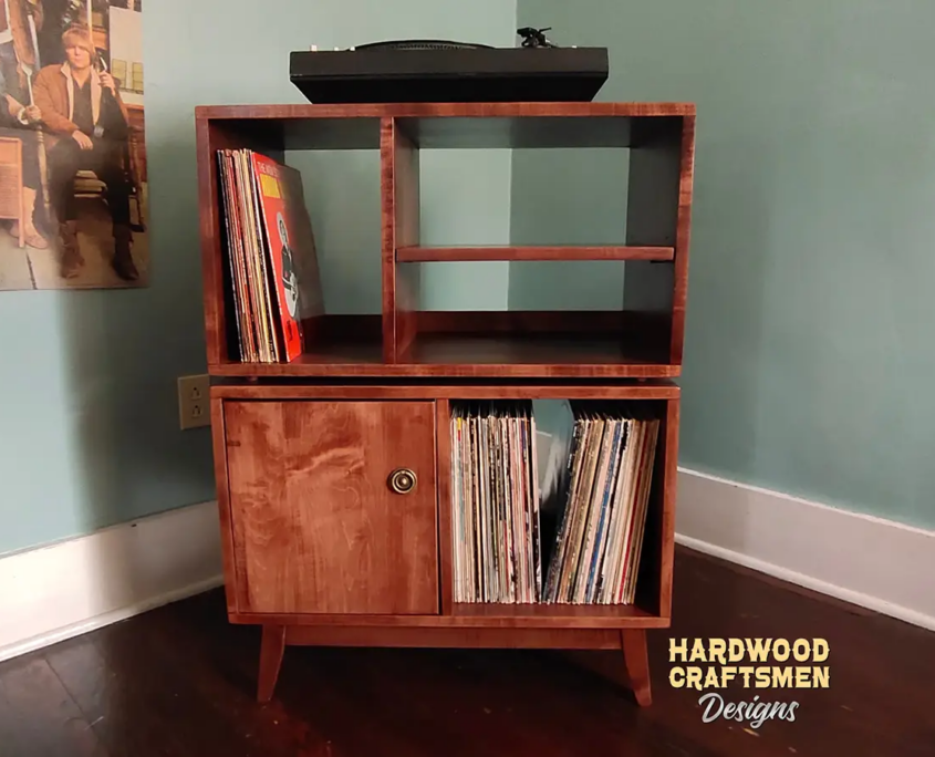 Large 2x2 solid wood record stand featuring a turntable shelf, two media shelves, four storage bins with a door on the bottom left, and tapered mid-century legs.