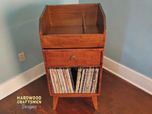 Tall solid cherry record cabinet featuring an upper vinyl flip bin. The lower section includes a drawer cabinet with one divided storage compartment, supported by tapered mid-century legs.