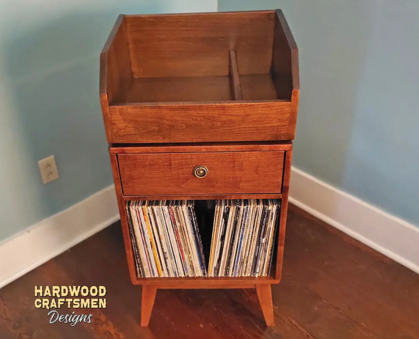 Tall solid cherry record cabinet featuring an upper vinyl flip bin. The lower section includes a drawer cabinet with one divided storage compartment, supported by tapered mid-century legs.