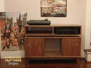 Large solid walnut media console, available from 42 to 72 inches, featuring an upper TV shelf. Below are two media compartments above three divided storage compartments, with two outer hardwood doors covering the side compartments, all on tapered mid-century legs.