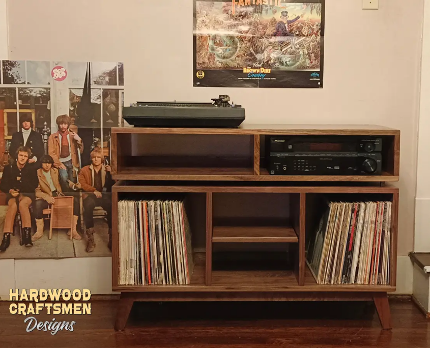 Large solid walnut media console, available from 42 to 72 inches, featuring an upper TV shelf. Below are two media compartments above three divided storage compartments, with a turntable shelf featured in the center compartment, all on tapered mid-century legs.